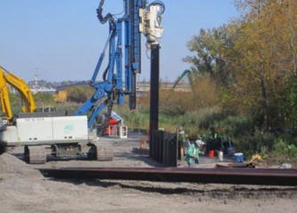 A vibratory hammer drives steel panels into the ground.