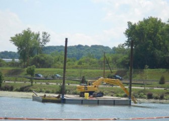 Large debris removal continues along the western shoreline of Onondaga Lake, with I-690 in the background.