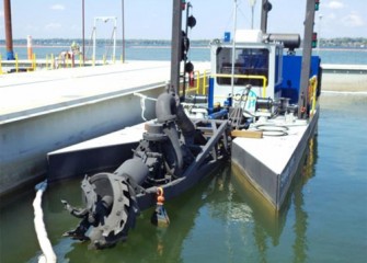 Small dredge moored at dock with cutter head visible.