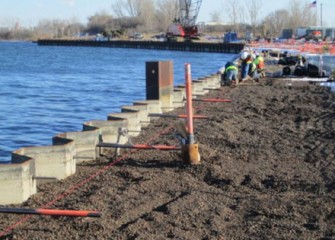 Workers install support structures behind the barrier wall.