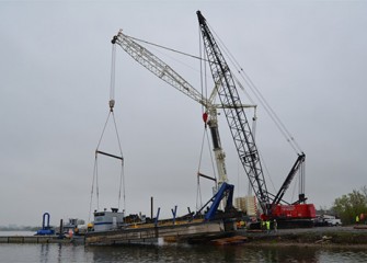 Two cranes safely place a dredge into the lake.