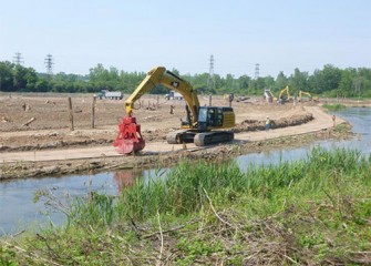 Buckets are used to pull up material from the creek; Geddes Brook wetlands are seen in the background.