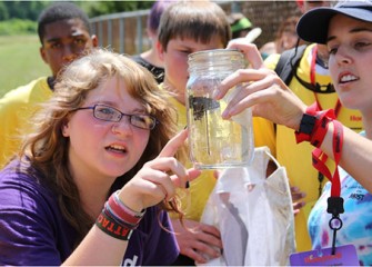 A student examines a butterfly with assistance from a team leader