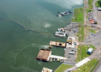 A hydraulic dredge operates close to shore (upper right). Barges at a dock are filled with cap material ready for placement on the lake bottom.