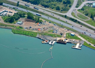 Material from the lake bottom is suctioned into a pipeline. Four booster stations push the material approximately four miles to the consolidation area. The first of four booster stations can be seen at the edge of shore.