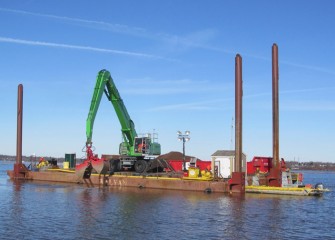 Cap material consisting of larger rocks is applied by equipment mounted on a barge.