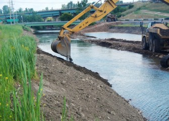 An excavator places topsoil along the shoreline. A seed mix of native plant species will be spread along the shoreline to prevent erosion and create habitat.