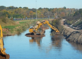 Crews use excavators in the middle of Nine Mile Creek to access both banks. I-690 can be seen in the background.