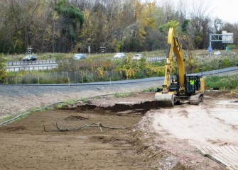 Topsoil is placed over the clay-like soil. The county’s western shoreline trail, under construction, is immediately to the left; I-690 is in the background.