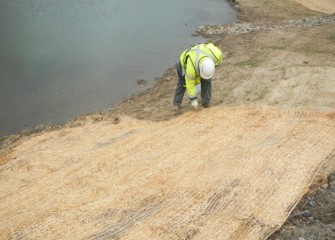 A worker places fresh erosion control blanket made of natural fibers along the banks.