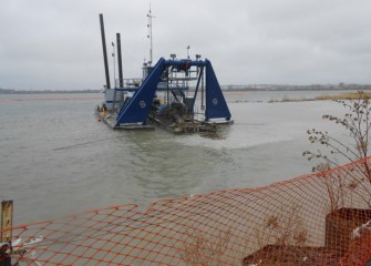 A dredge removes lake bottom material near the barrier wall (lower right corner).  Plans are to complete dredging in 2014, a year ahead of schedule.