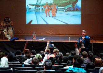 Students ask questions as Dr. Thomas speaks about his experience in space and preparing for a career in science. The background photo shows Thomas after returning from one of his shuttle missions.