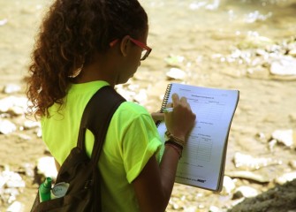 Student Bianca Melendez Martineau from Manlius Pebble Hill School records stream velocity measurements in her workbook.