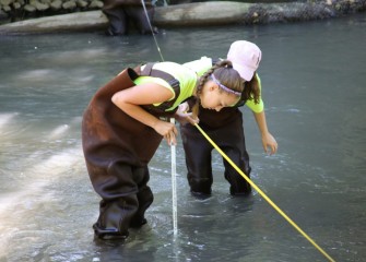 Lauren Hurd (left) from Solvay Middle School measures depth and stream velocity near the center of Onondaga Creek with help from Katherine Baldwin.