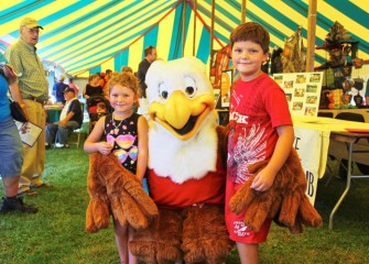 Teagan (left) and Mason Wojieck, from Red Creek, pose with “Eddie the Eagle,” National Rifle Association’s safety program mascot, in one of the display tents.