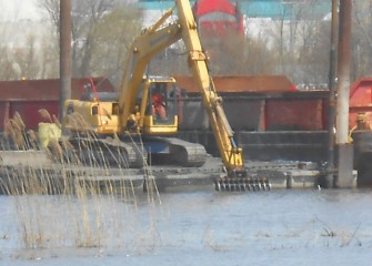 An excavator with a rake attachment is used to lift old tires out of the lake.