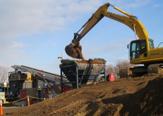 Sand is placed into a hopper before traveling up a conveyor where it is weighed and sent into a tank to mix with other cap material.