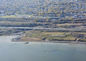 A capping barge works along the shoreline near the mouth of Harbor Brook.