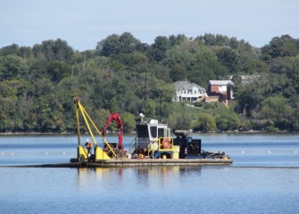 A worker on a support boat adjusts a capping line used to transport capping material mixed with water to the hydraulic capping barge.