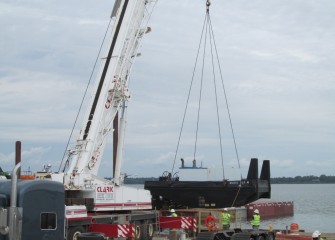 A hydraulic truck crane is used to lift a section of a tug boat into the water.