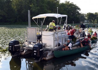 Canoeists unload water chestnut to a support boat operated by Onondaga Lake Conservation Corps corporate partner Anchor QEA.
