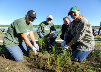 First-time volunteers Melanie Tracy (left), Julie Harsma (right back) and Kourtnie Clark (right), all from Syracuse, plant switchgrass with habitat expert Joe McMullen.