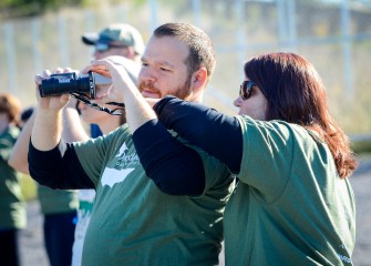 Matthew and Elizabeth Tognarelli, graduate students at Syracuse University, use a phone to capture an image of a Great Egret through binoculars.