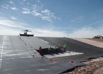 Polyethylene liner is unrolled down a slope of the consolidation area. The liner is 40 mil (thousandths of an inch) thick, a little over one millimeter.