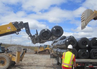 Work resumes covering the consolidation area. Rolls of geocomposite drainage net are unloaded and stacked at the site.