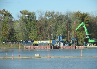 The telestacker places new lake bottom material near the mouth of Nine Mile Creek. Mats are used in shallow areas (foreground) to provide access for topsoil placement.