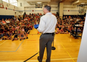 Honeywell Syracuse Program Director John McAuliffe speaks to students at East Syracuse Elementary’s final assembly of the school year before presenting a flight suit.