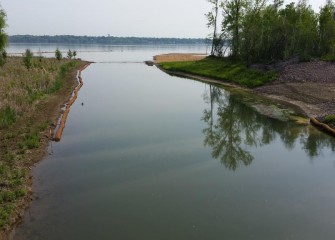 Biodegradable coir logs are placed along the banks of Nine Mile Creek to protect soil and plants from wave erosion. The logs may be made of coconut or aspen fibers, straw, or other natural materials. A temporary road into the creek (right) is used in capping operations.