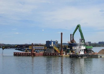 A small tugboat (foreground) is used to move the telestacker and support barges into position.