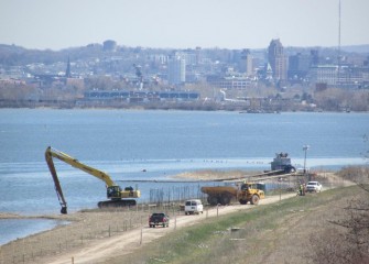 Topsoil placement continues along the western shoreline of Onondaga Lake. Fencing is set up to protect plantings; a pump is positioned for irrigation needs.