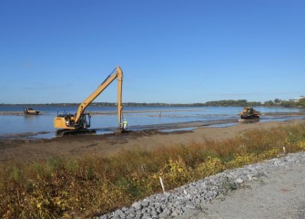 A long stick backhoe places topsoil along the southwestern shoreline.