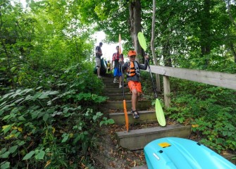 Grant Clift, age 8, from Baldwinsville, carries kayak paddles down to the creek shoreline.