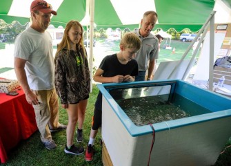 Honeywell Syracuse Program Director John McAuliffe (right) looks at fish from Onondaga Lake with the Abbott family of Nedrow.