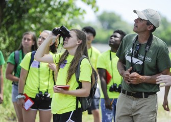 Montezuma Audubon Center Director Chris Lajewski helps Ruth Melnik, from West Genesee Middle School, and other members of Team Purple, identify bird species near the outlet of Harbor Brook to Onondaga Lake.