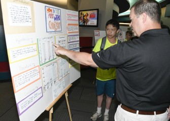 Aiden Lee, from Wellwood Middle School, shows a visiting parent his group’s findings on water chemistry.